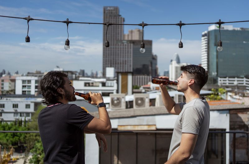 Two men enjoying beers on a city rooftop, fostering friendship in an urban setting.