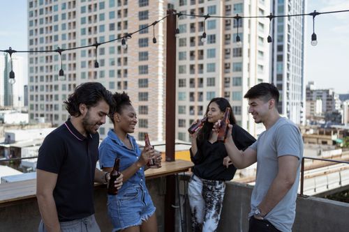 Free A group of friends enjoying drinks on a rooftop with a cityscape view, creating a vibrant social atmosphere. Stock Photo