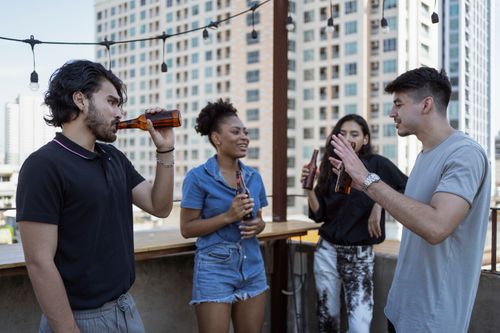 Free Group of friends enjoying drinks and conversation on a rooftop terrace with city skyline view. Stock Photo