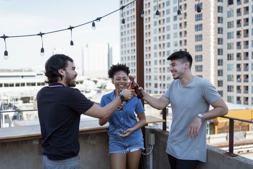 Free Three friends enjoying a casual toast on a rooftop balcony with cityscape in the background. Stock Photo