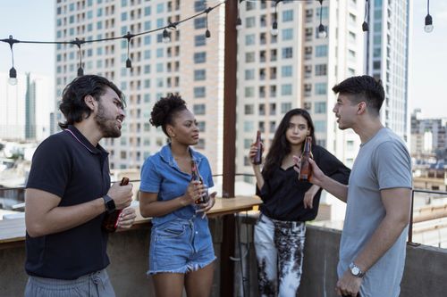 Free Friends socializing with bottles of beer on an urban rooftop setting. Stock Photo