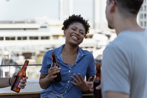 A Smiling Woman in Denim Shirt Holding a Beer Bottle