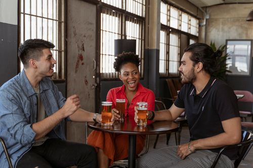 Free A diverse group of friends enjoying drinks and laughter at an indoor cafe setting. Stock Photo