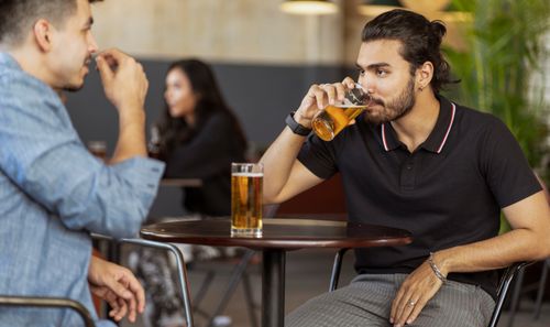 Free Men conversing and enjoying drinks at a pub, creating a relaxed social atmosphere. Stock Photo