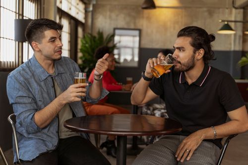 Free Two men enjoy a lively discussion over beers at a stylish indoor cafe setting. Stock Photo