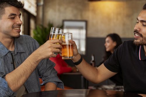 Free Two friends enjoying a casual toast over beers, indoors with a warm atmosphere. Stock Photo