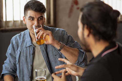 Man in Blue Denim Long Sleeve Shirt Drinking Beer of Clear Drinking Glass