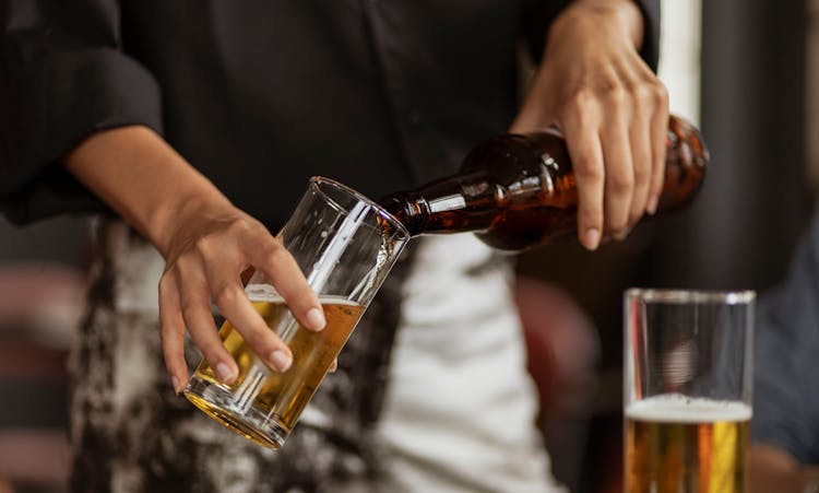 A Person Pouring Beer On A Clear Drinking Glass