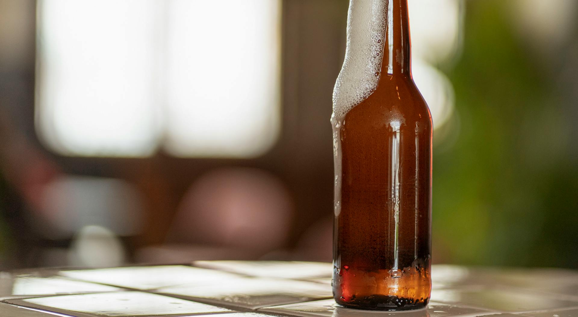 A Brown Glass Bottle with Beer Foam on the Table