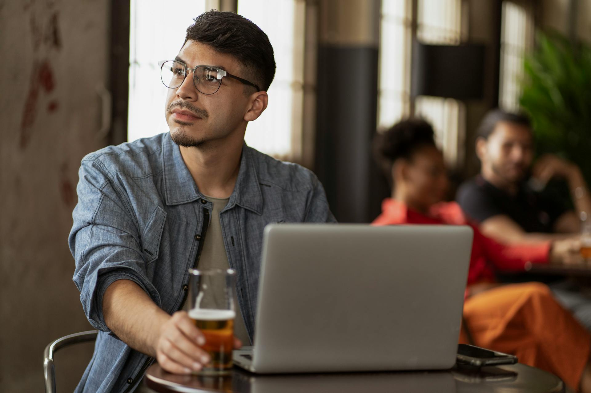 Man relaxing with a beer while using a laptop in a cozy cafe setting, enjoying downtime.