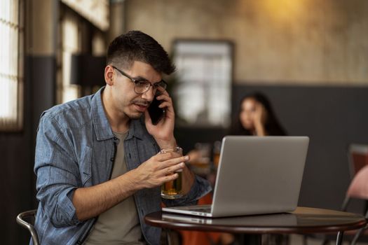 Man multitasking with laptop and phone while enjoying a drink in a cozy café.