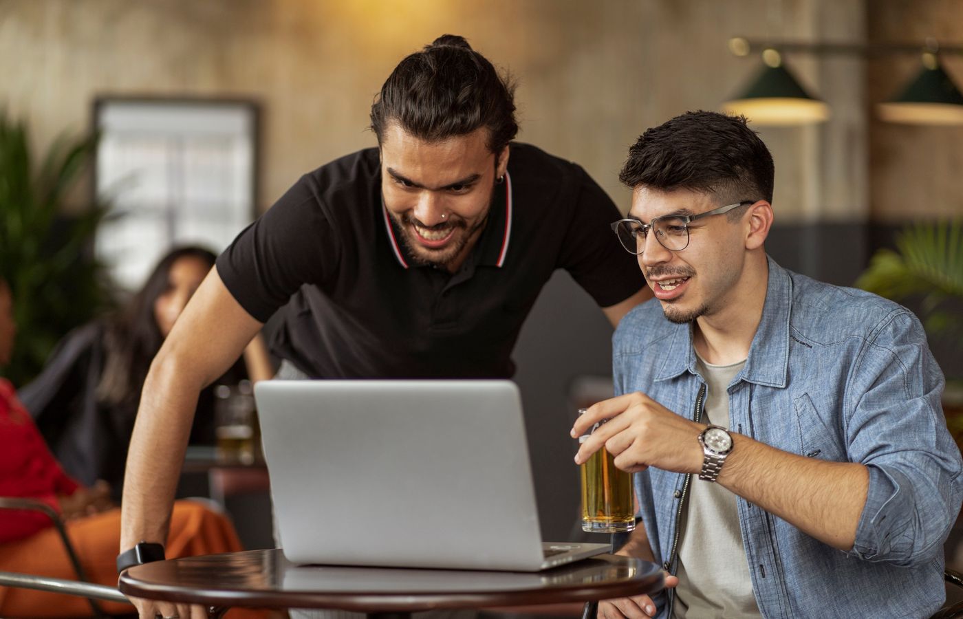Two men enjoying a casual meeting in a cafe, sharing laughs and drinks over a laptop.