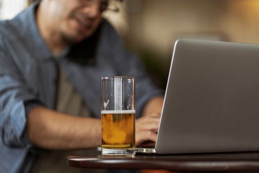 一名男子在室内一边用笔记本电脑远程工作，一边享用一杯啤酒