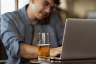 男人一边用笔记本电脑工作，一边喝着啤酒，专注于多任务处理