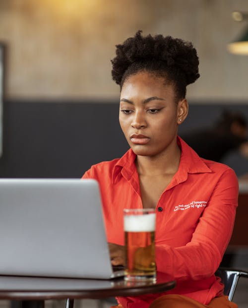 Woman Sitting at Table with Laptop and Glass of Beer