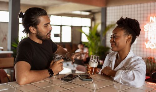 Free Two friends chatting over drinks at a modern bar setting, enjoying their time together. Stock Photo