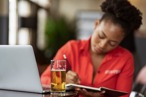 Woman Taking Notes with Open Laptop with Glass of Beer on Table