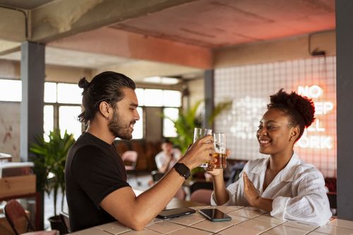 Free Two friends smiling and toasting with drinks at a modern indoor space. Stock Photo