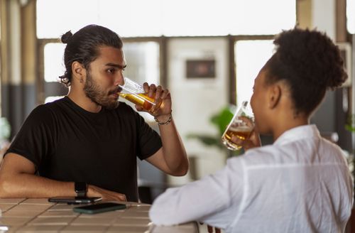 Free Two adults enjoying drinks and conversation at a bar setting. Stock Photo