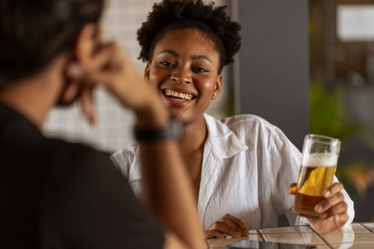 Woman Holding A Glass Of Beer, Talking To A Man And Smiling 