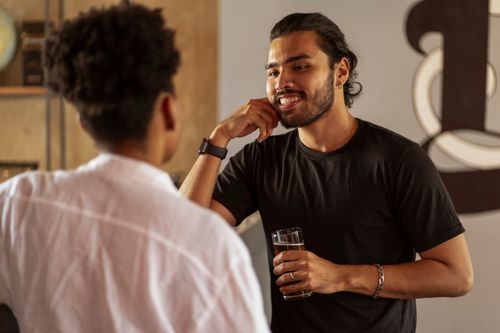Free Two friends having a casual conversation indoors, one holding a drink. Stock Photo