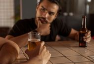 一名男子在酒吧里拿着啤酒瓶若有所思，正在与人交谈