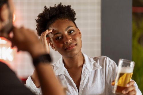 Free A woman with short black hair holding a glass of beer, smiling sincerely in a casual indoor setting. Stock Photo