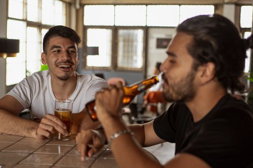 Free Two men sitting at a bar counter sharing a casual drink and enjoying their time together. Stock Photo