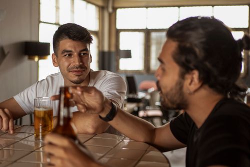 Free Two men chatting over beer indoors, enjoying a relaxed atmosphere. Stock Photo