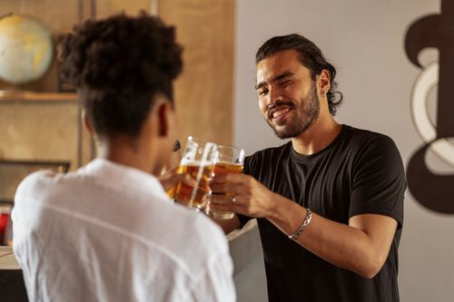 Free Two friends in a bar sharing a moment with beers, smiling and talking. Stock Photo