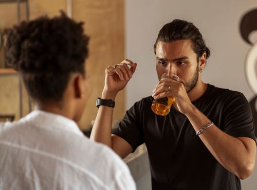 Free A young man sipping beer while engaging in a conversation indoors. Stock Photo