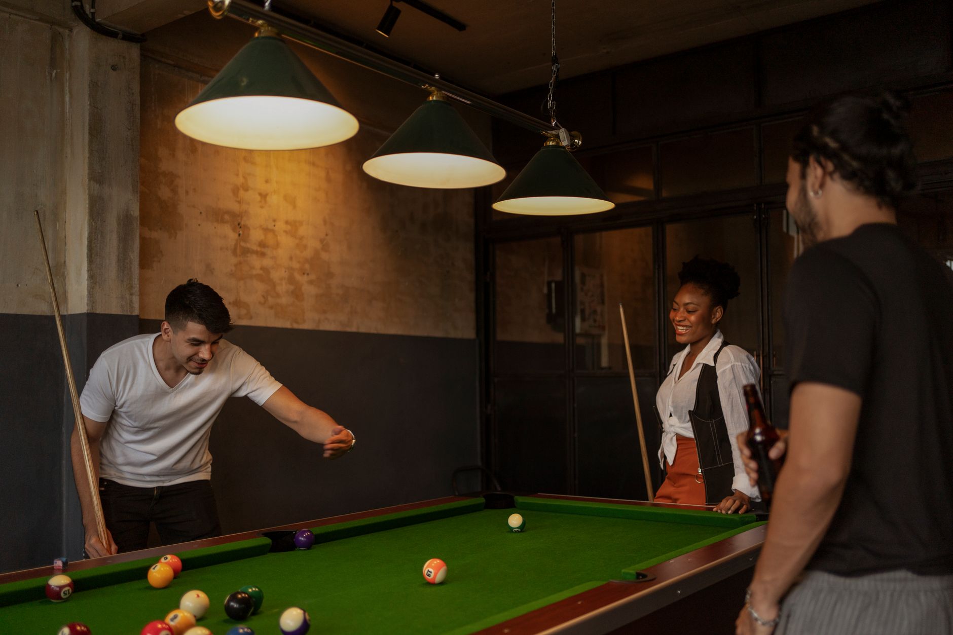 Three adults enjoying a casual game of pool in a cozy, dimly-lit bar environment.