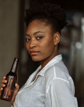 Portrait of a confident young woman holding a beer bottle indoors.