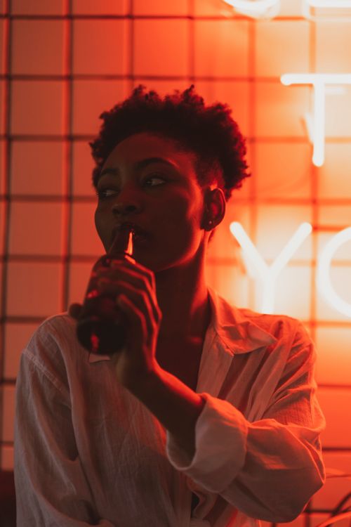Free A contemplative portrait of a person with a beer bottle against a neon red backdrop. Stock Photo