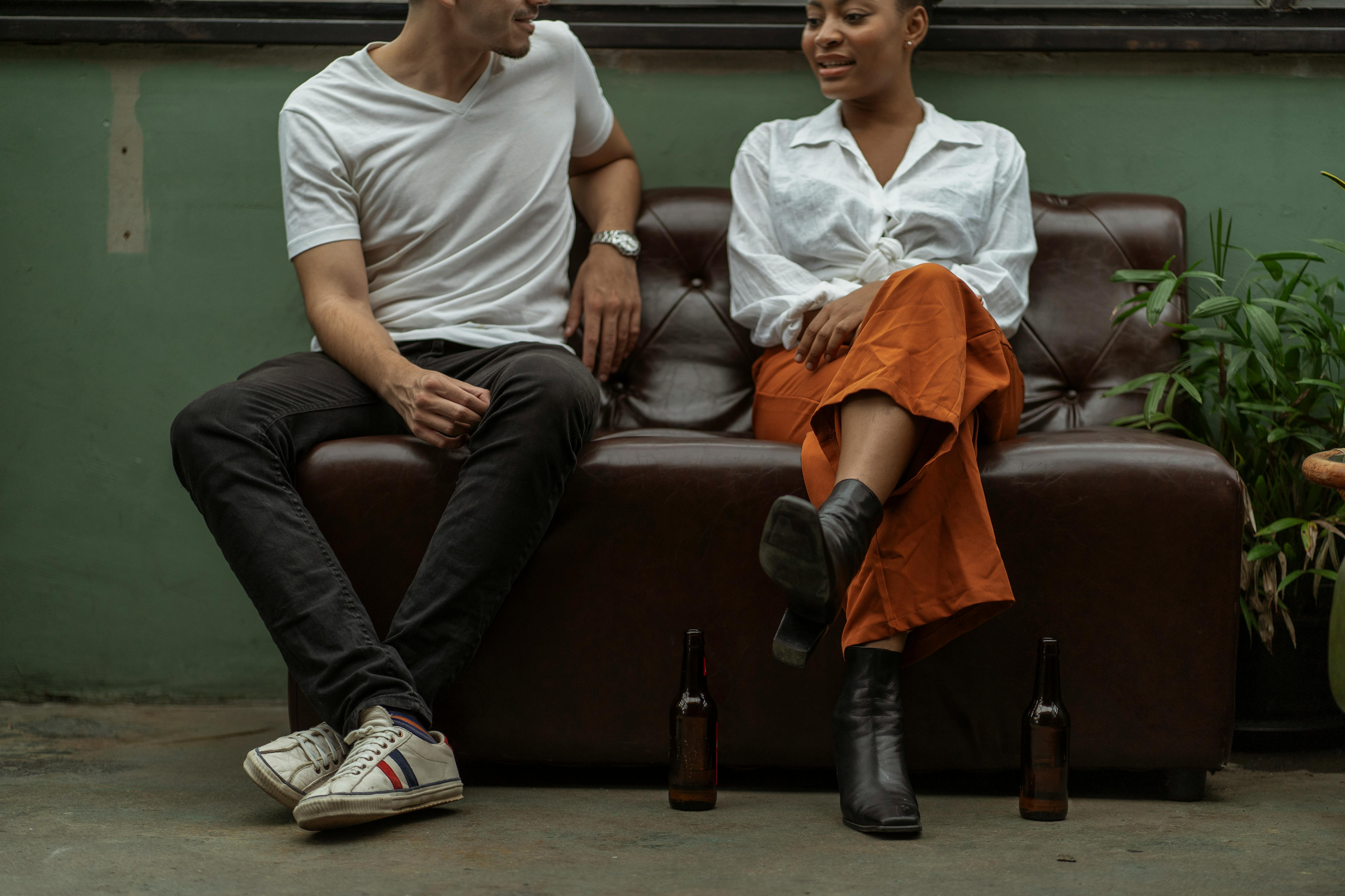 Free A man and woman talking casually on a leather couch with drinks beside them indoors. Stock Photo