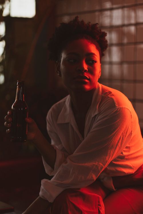 Free Stylish portrait of a woman in warm lighting holding a drink, conveying a moody atmosphere. Stock Photo