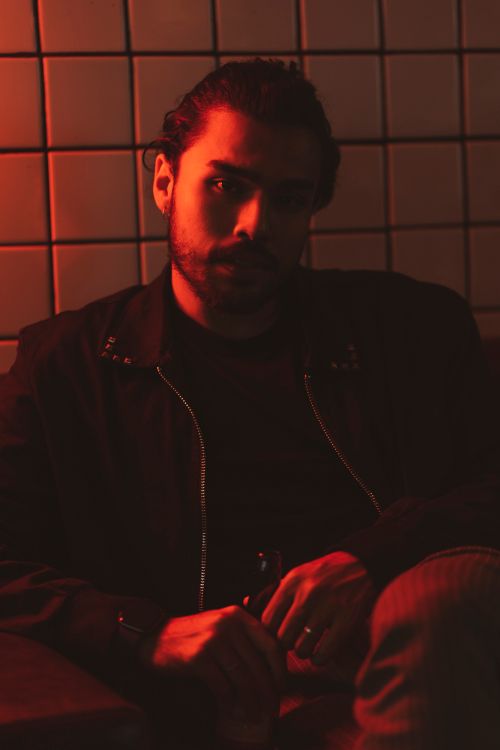 Free A man sitting in a dimly lit club with warm red lighting, creating a moody atmosphere. Stock Photo