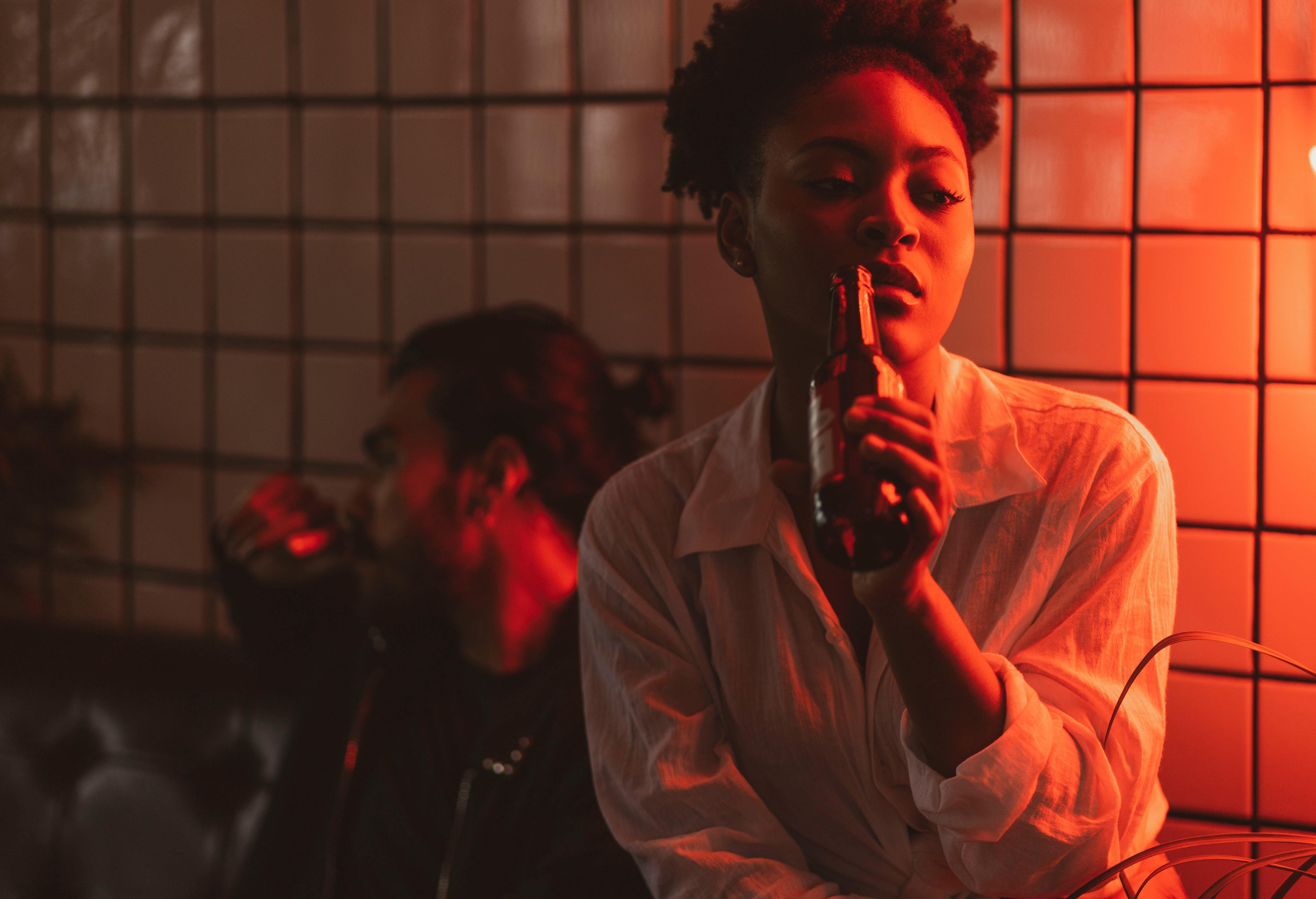 Two adults enjoying drinks in a dimly lit, stylish bar with red lighting.