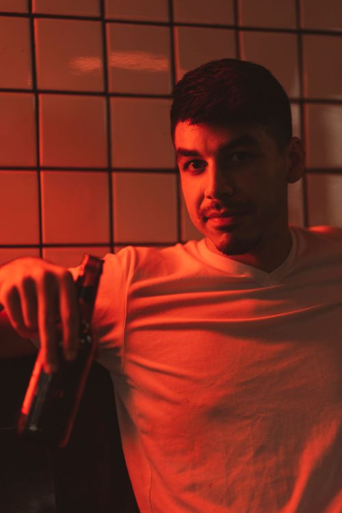 Free Portrait of a man casually sitting and enjoying a beer in warm ambient light. Stock Photo