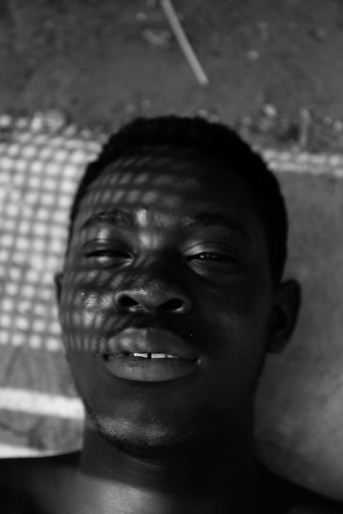 Free Black and white from above of African American male with short hair looking at camera while lying on ground under shadows of net on face Stock Photo