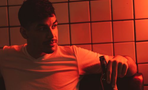 Free A thoughtful man in a dimly lit room holding a beer bottle, in warm tones. Stock Photo