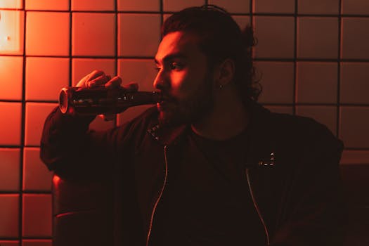 剪影：一名男子在灯光昏暗、红灯闪烁的房间里对瓶饮酒，非常适合夜生活主题