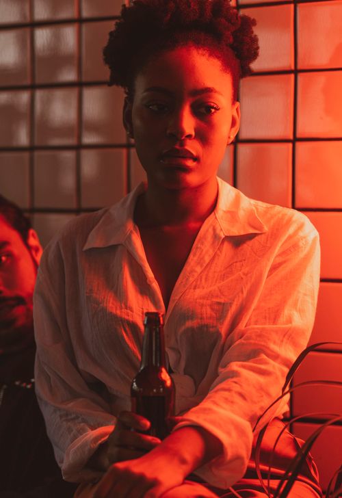 Free An artistic photo of a woman holding a bottle under neon red light indoors. Stock Photo