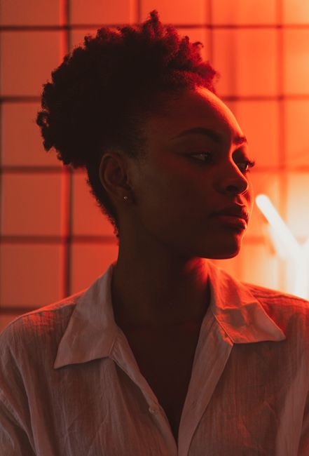 Profile of a young woman in neon red lighting, showcasing style and mood in a creative setting.