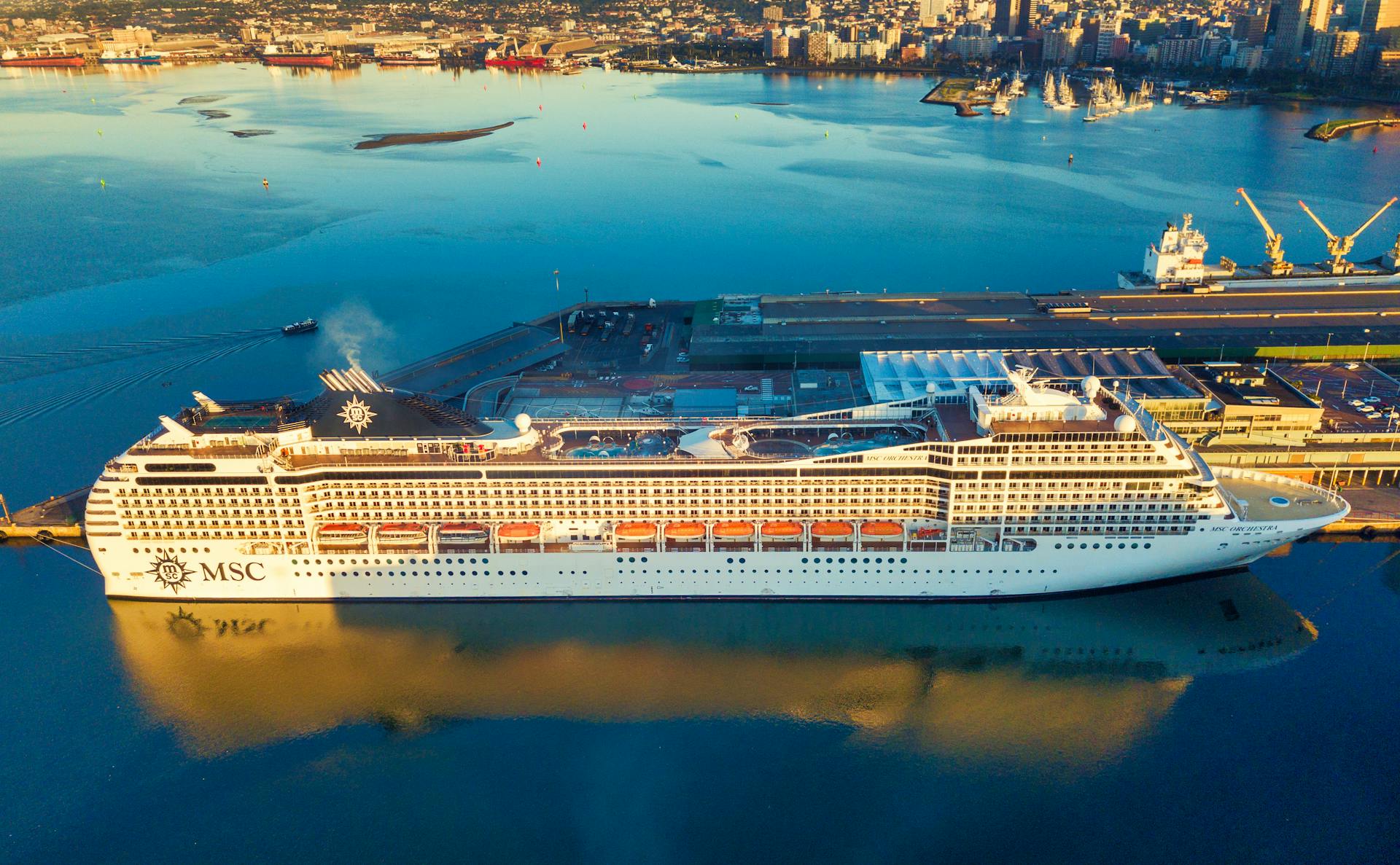 Aerial view of a cruise ship docked at a South African harbor with city skyline.