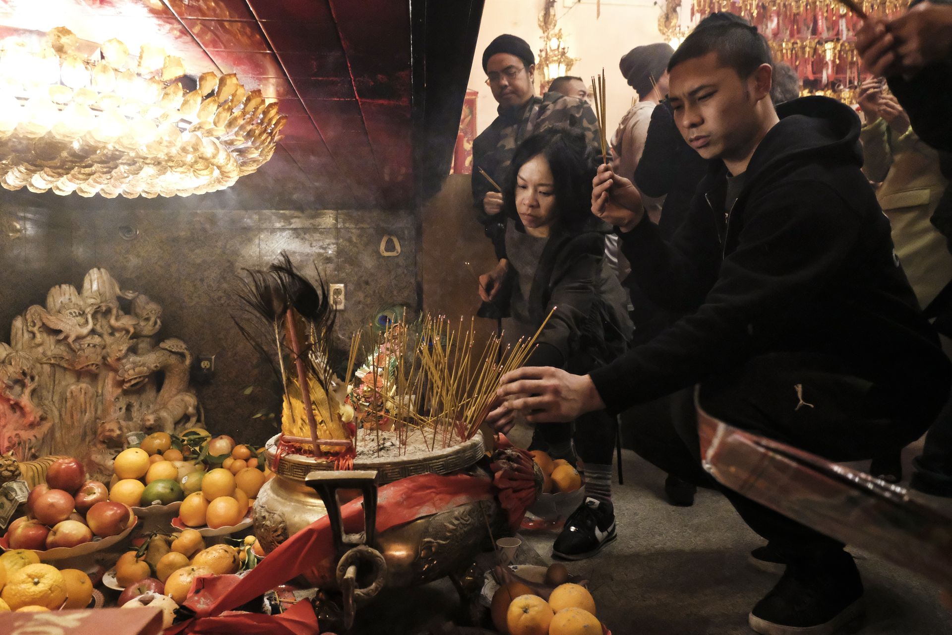 People participate in a spiritual ceremony with incense and fruit offerings, highlighting traditional culture.