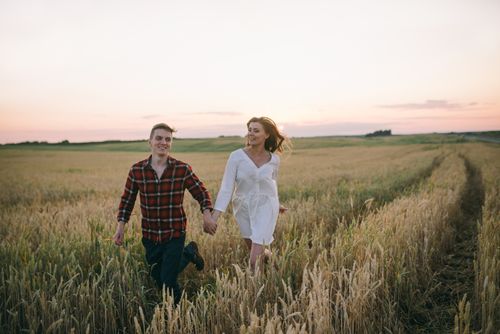 Free Romantic couple holding hands while running in a wheat field at sunset. Stock Photo