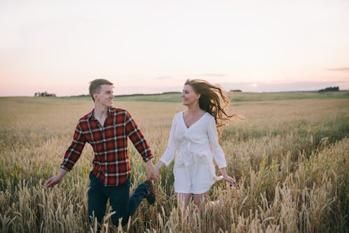 A Couple Running on a Wheat Field while Looking at Each Other