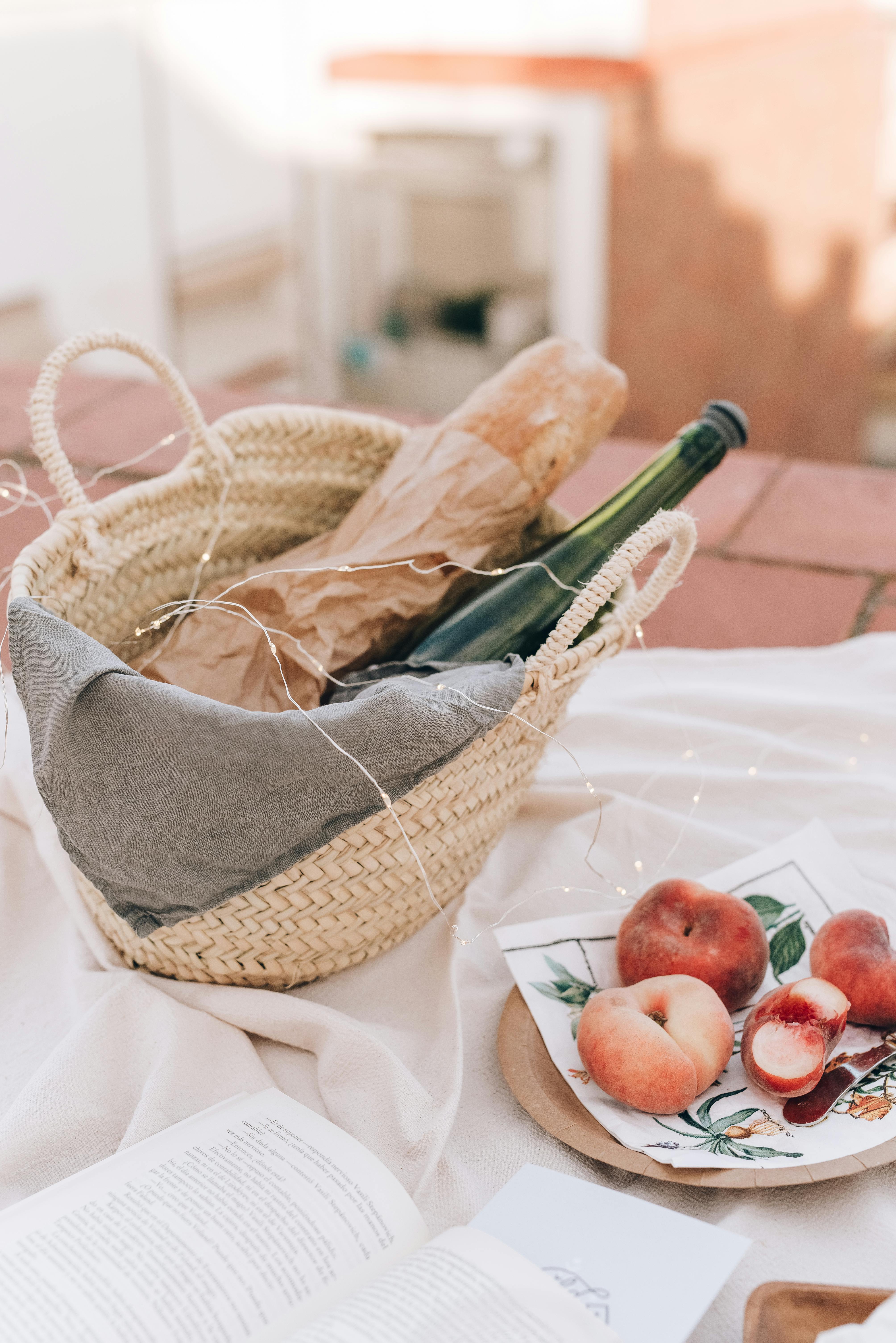 Cozy summer picnic scene with a wicker basket, wine, baguette, and fresh peaches.