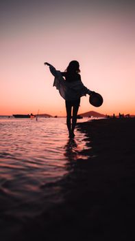 A woman in silhouette gracefully walks along the İzmir beach during a vibrant sunset.